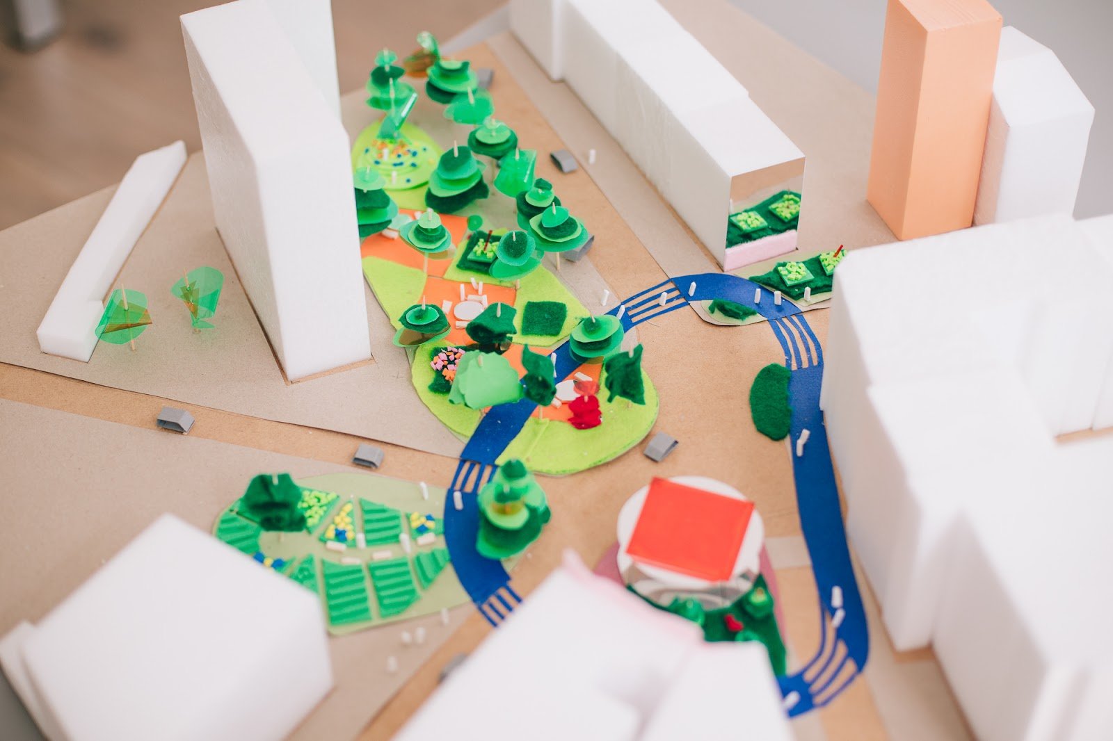  A close-up of a city model made of cardboard. There are large, white skyscrapers and colorful lawns, trees and walking routes.