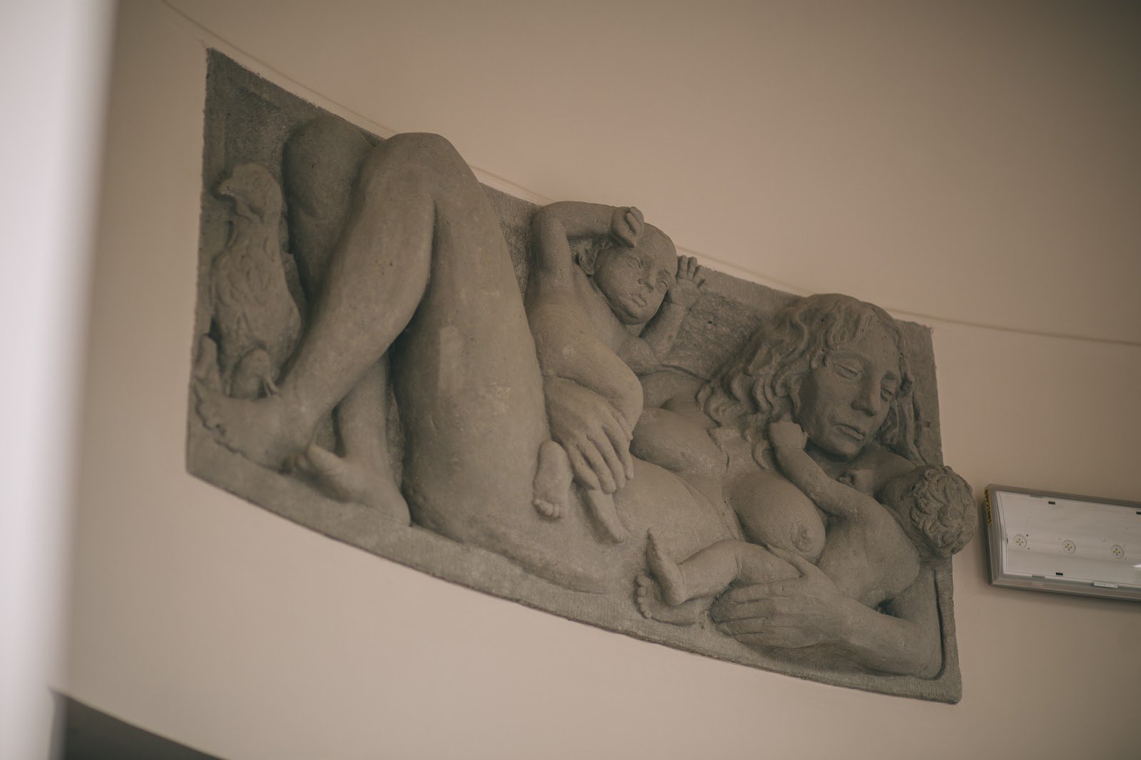 Kolorowa, pozioma fotografia przedstawiająca kamienną płaskorzeźbę leżącej kobiety z dwójką dzieci.