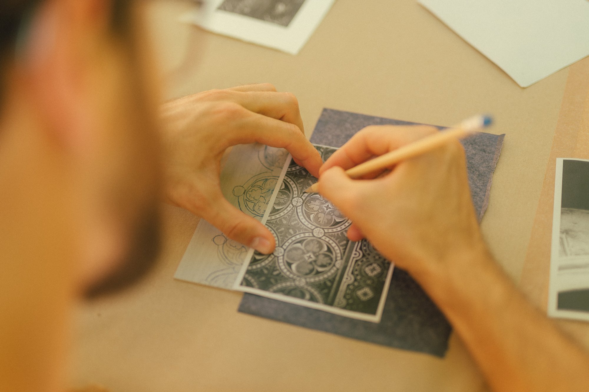 Kolorowa, pozioma fotografia na której widać ujęcie pracy podczas warsztatu z linorytu. Obrócony plecami do obiekty młody mężczyzna rysuje elementy dekoracyjne z pieca kaflowego.