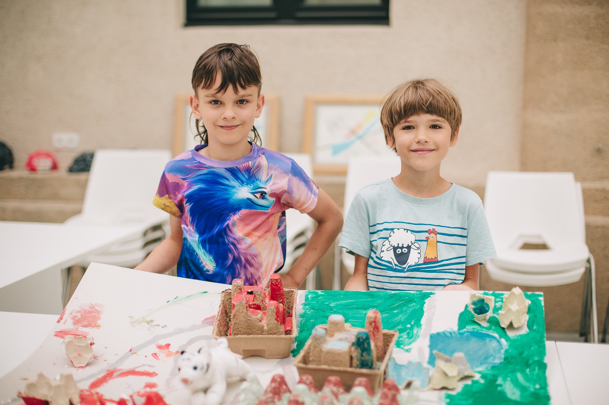 Dwuch kilkuletnich chłopców z dumą prezentuje wykonaną przez siebie makietę z kartonowych elementów.
