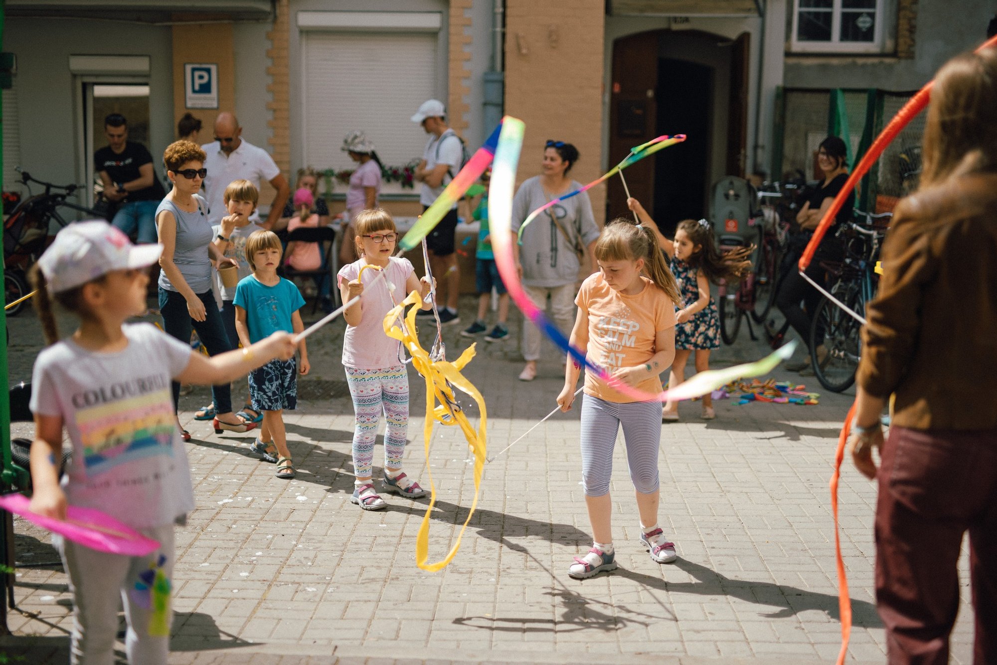 Pozioma, kolorowa fotografia przedstawia grupę dzieci w różnym wieku bawiących się szarfami.