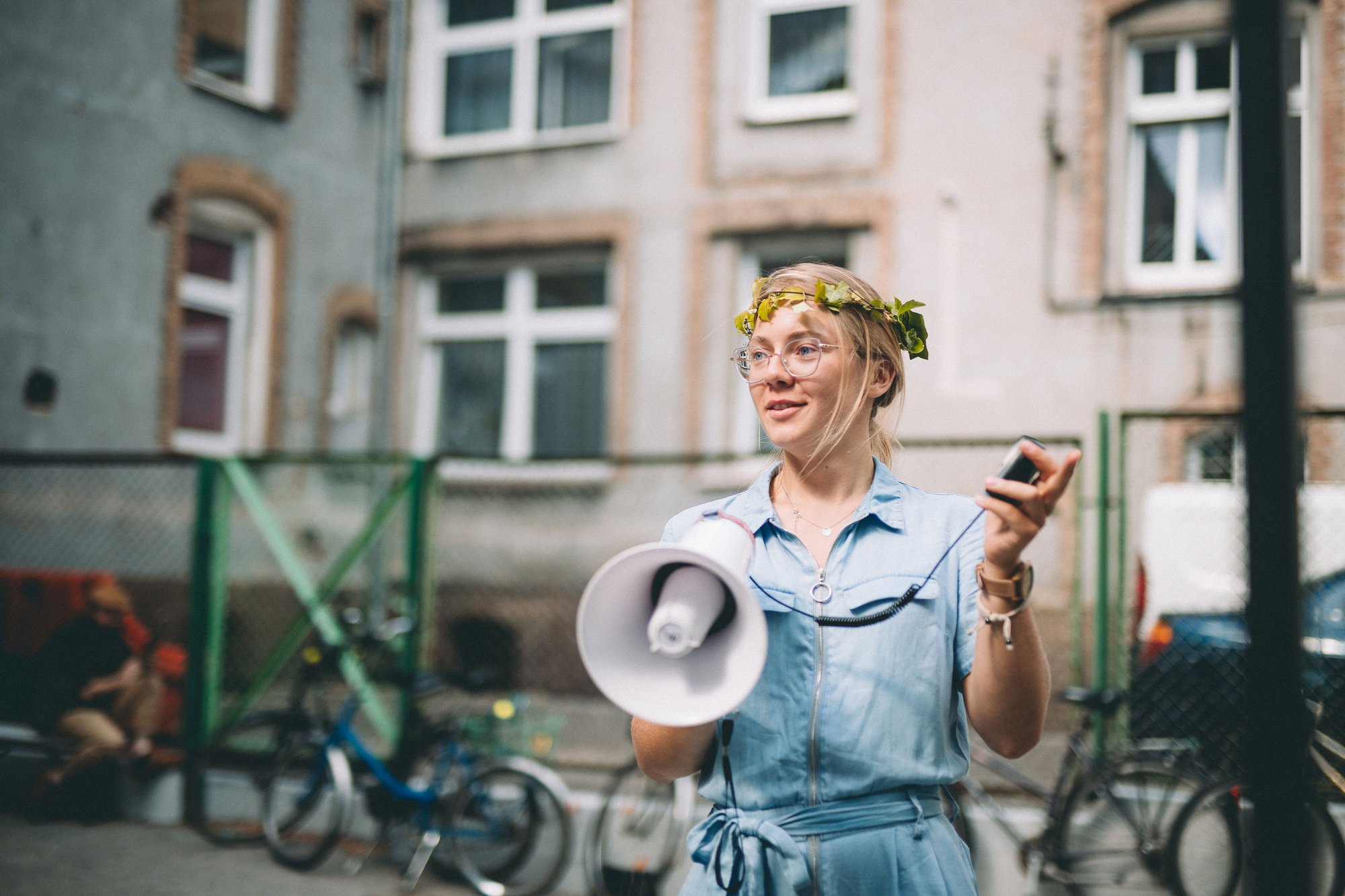 Młoda kobieta z wiankiem na głowie i megafonem w ręce stoi przed budynkiem naszej siedziby przy ulicy Curie-Skłodowskiej 63a.