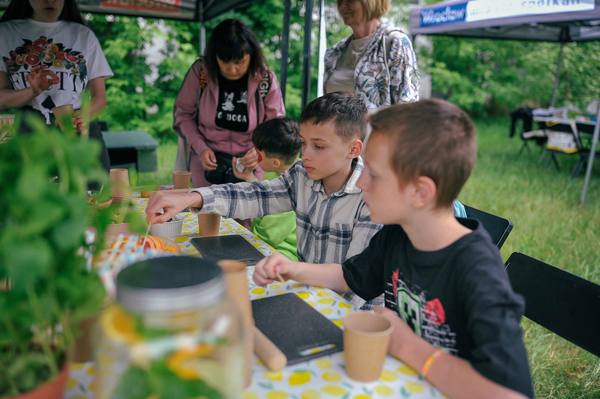 Kolorowa fotografia wykonana podczas pikniku osiedlowego. Przy dużym stole siedzi grupa dzieci, trwają warsztaty.