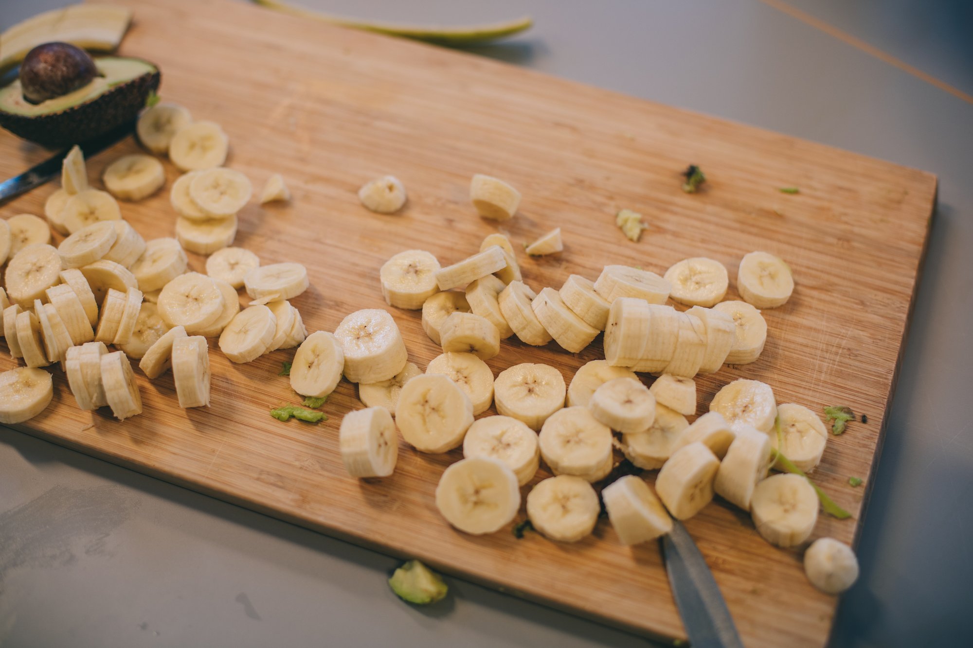 Zbliżenie na pokrojone banany leżące na drewnianej desce. Obok bananów leży rozkrojone awokado.