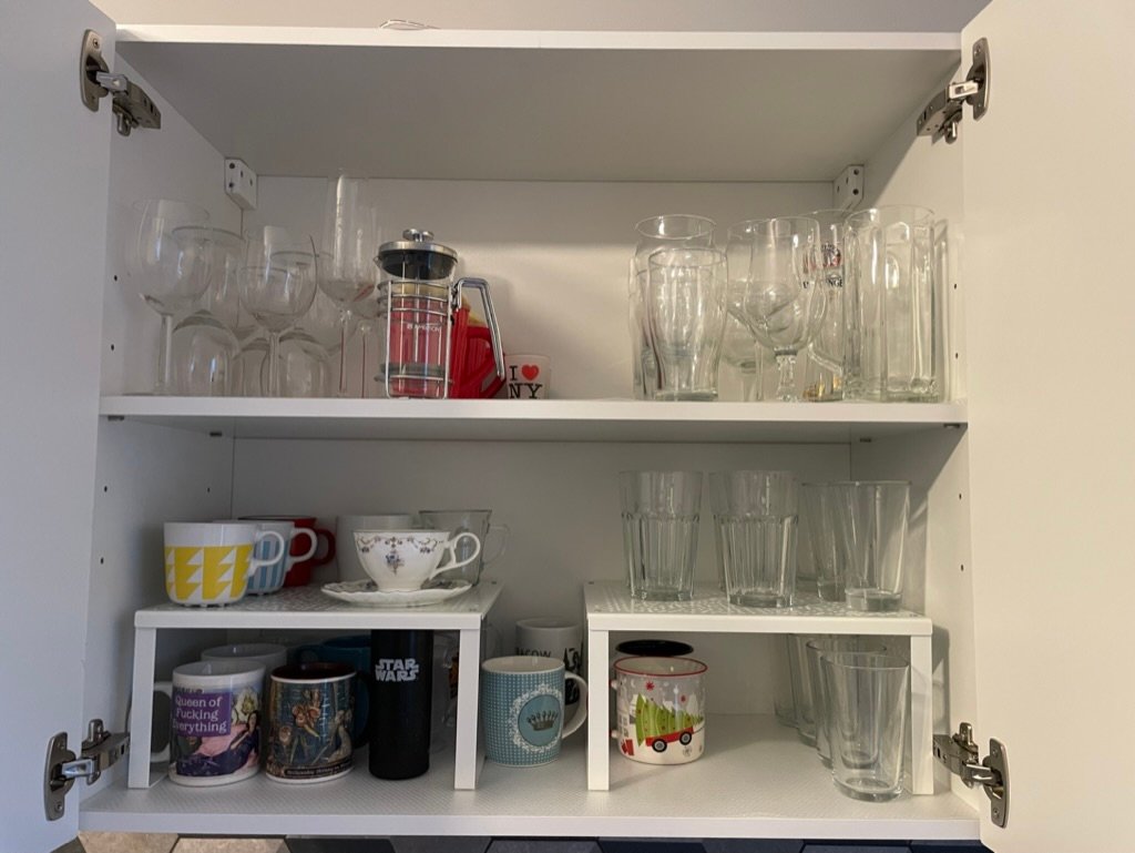 Kolorowa, pozioma fotografia: wnętrze szafki kuchennej z kubkami i szklankami. Wszystkie przedmioty są uporządkowane, w szafce jest czysto i przestronnie.