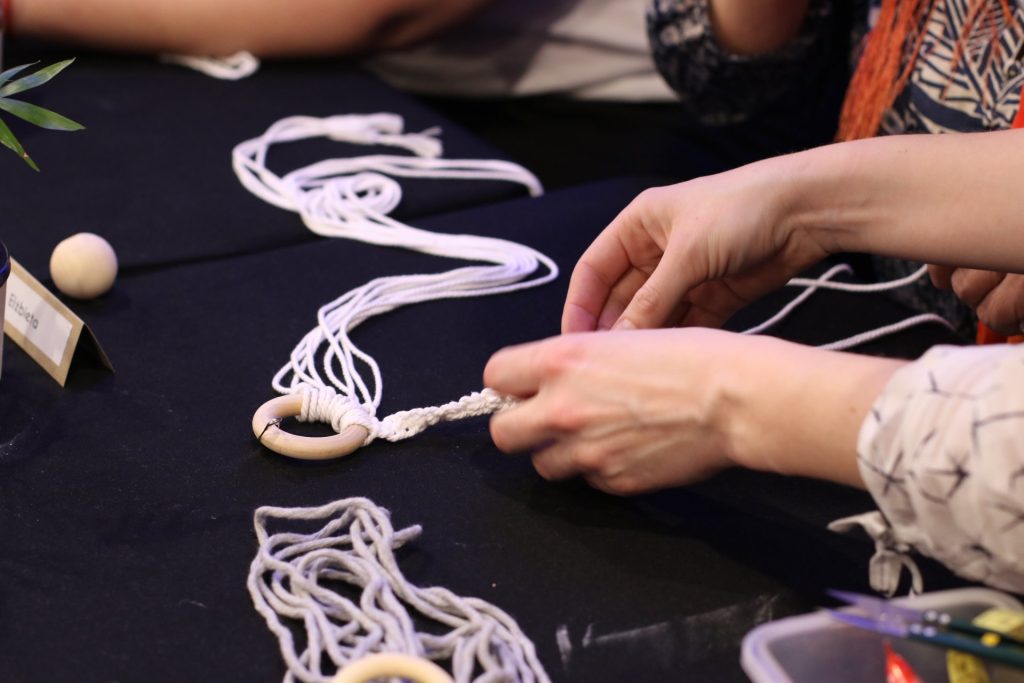 materiały organizatora Kolorowa fotografia: zbliżenie na dłonie wykonujące kwietnik z jasnego sznurka.
