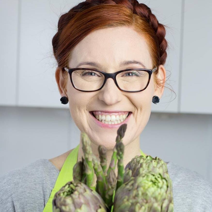 materiały organizatora Kolorowa fotografia przedstawia zbliżenie na twarz Katarzyny Gubały. Kobieta jest szeroko uśmiechnięta, rudy warkocz ma upięty wokół głowy, a przed sobą trzyma bukiet ze szparagów i karczochów.