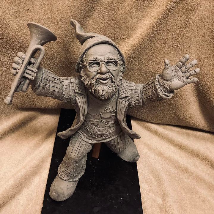 Kolorowa fotografia przedstawia figurkę Krasnala Siwka - ma okulary i krótką brodę, a w prawej dłoni trzyma trąbkę.