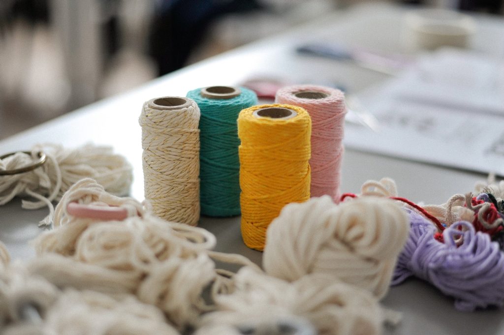 zdjęcie: Anna Pazdej Kolorowa fotografia przedstawia zbliżenie na stojące na stole kolorowe szpulki nici: białe, żółte, zielone i różowe.