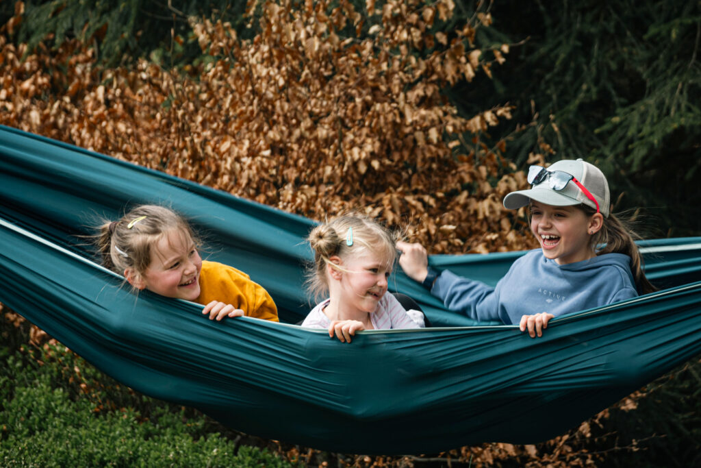 zdjęcie: Marcin Trzpiot Kolorowa fotografia przedstawia trójkę dzieci siedzących w dużym hamaku, rozwieszonym między drzewami.