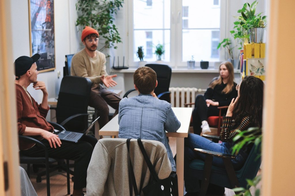zdjęcie: Marcin Szczygieł Kolorowa, pozioma fotografia: w jasnym pomieszczeniu przy dużym stole siedzi grupa młodych osób, które dyskutują ze sobą.