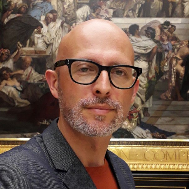 Kolorowa fotografia przedstawia mężczyznę w okularach z siwym zarostem.