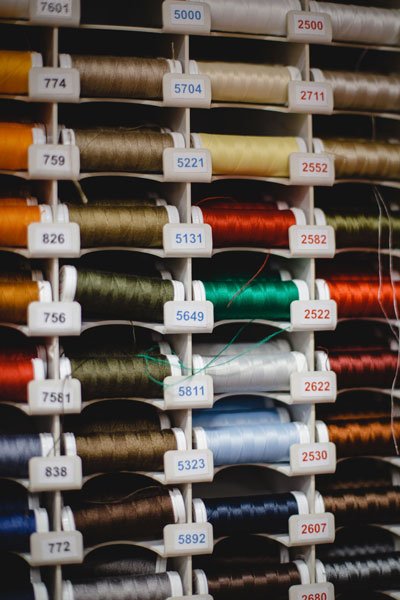 Zbliżenie na regał z kolorowymi nićmi. Każda rolka ma przypisany do koloru odpowiedni numer.