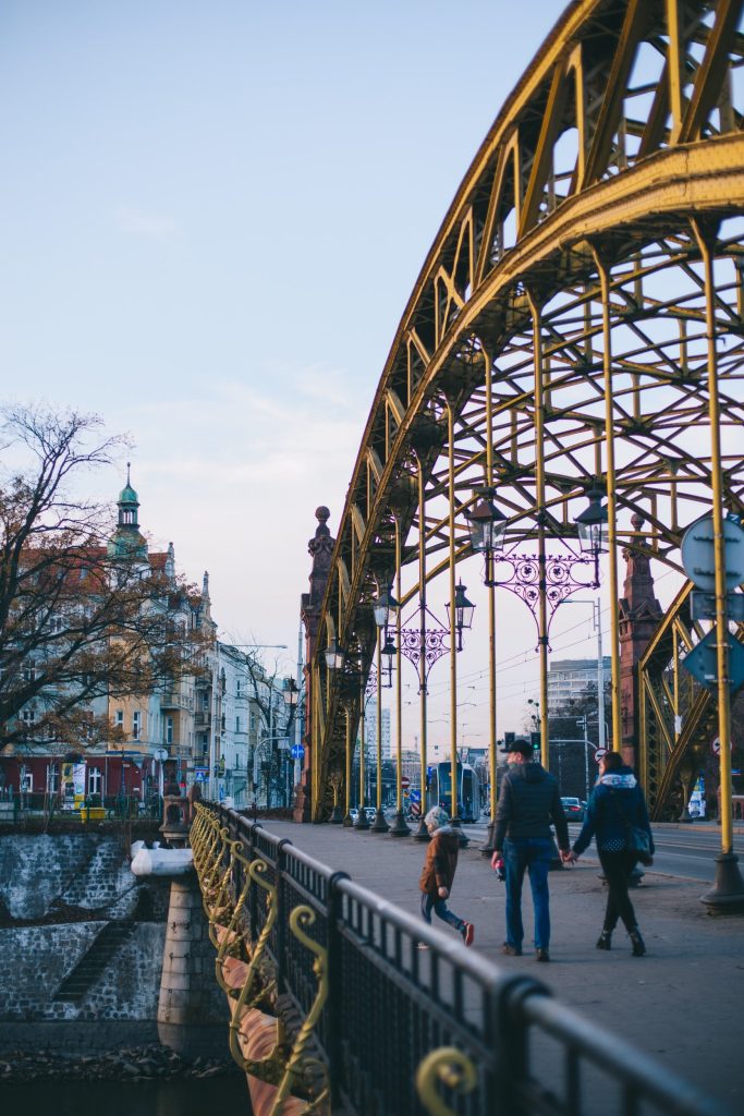 Trzy osoby spacerują po pięknie zdobionym moście Zwierzynieckim. 