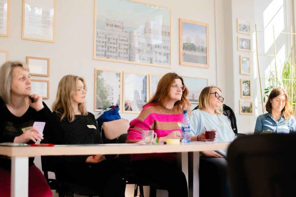 zdjęcie: Paweł Rychert Kolorowa fotografia przedstawia grupę kobiet w różnym wieku siedzącą przy stołach w jasnym pomieszczeniu. Trwa warsztat.