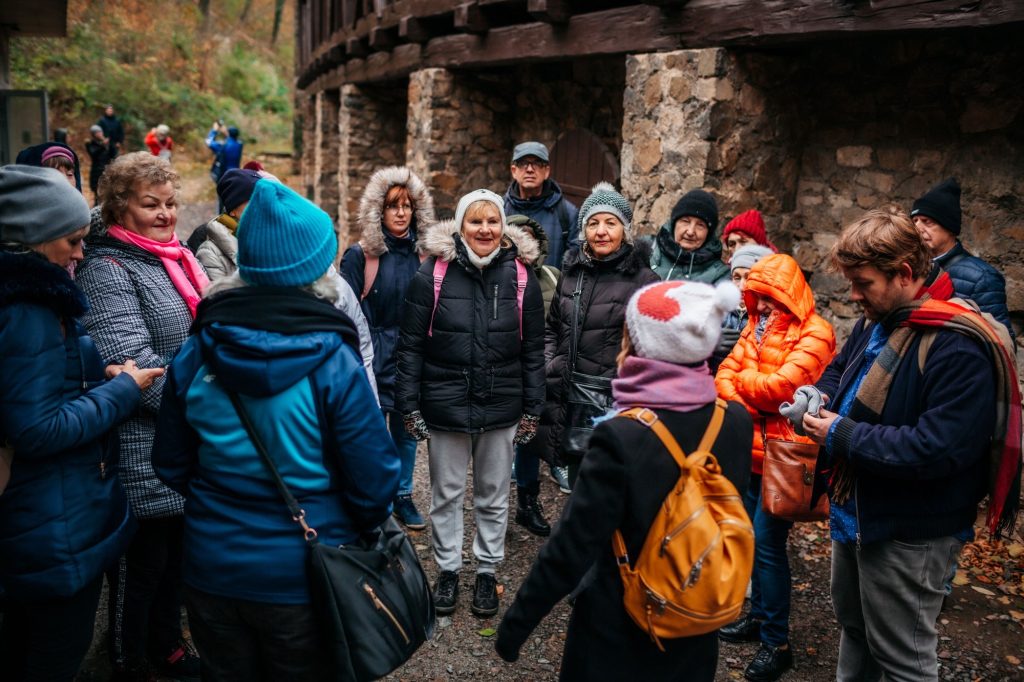 zdjęcie: Kalina Żaczek Kolorowa, pozioma fotografia: grupa seniorów i seniorek słucha opowieści o historii Zamku Książ. Zaraz rozpoczną zwiedzanie.