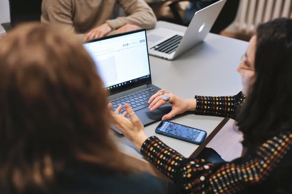 Kolorowa, pozioma fotografia: w pomieszczeniu przy stole warsztatowym siedzą trzy osoby, przed nimi leżą otwarte laptopy. Osoby dyskutują. Trwają prace nad kampanią do WBO.