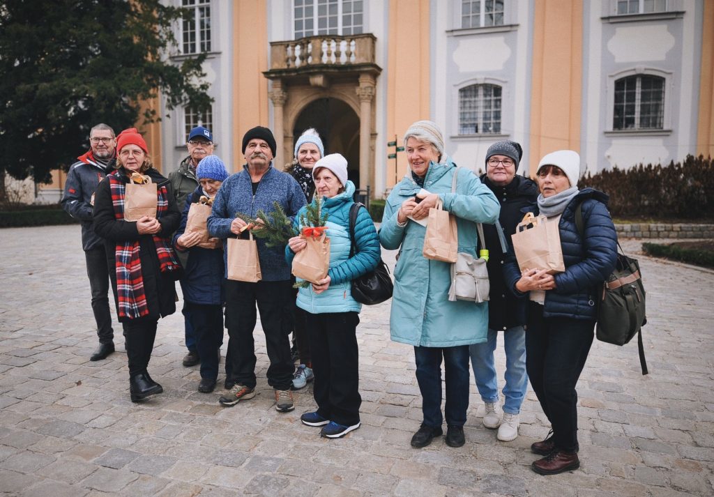 Kolorowa, pozioma fotografia: grupa seniorów i seniorek pozuje do zdjęcia pod Zamkiem w Wałbrzychu.