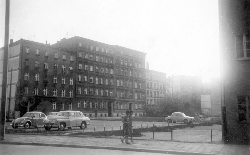 Czarno-biała archiwalna fotografia przedstawia dwie młode kobiety idące ulicą Hoene-Wrońskiego koło parkingu PWr.