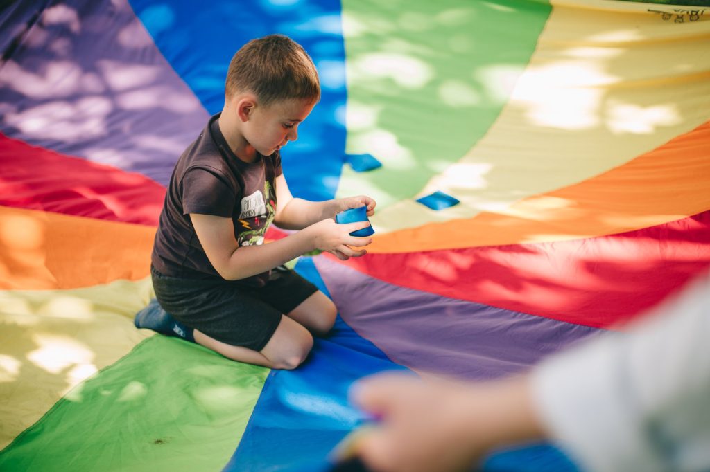 Kolorowa, pozioma fotografia. Kilkuletni chłopiec siedzi na kolorowej chuście animacyjnej.