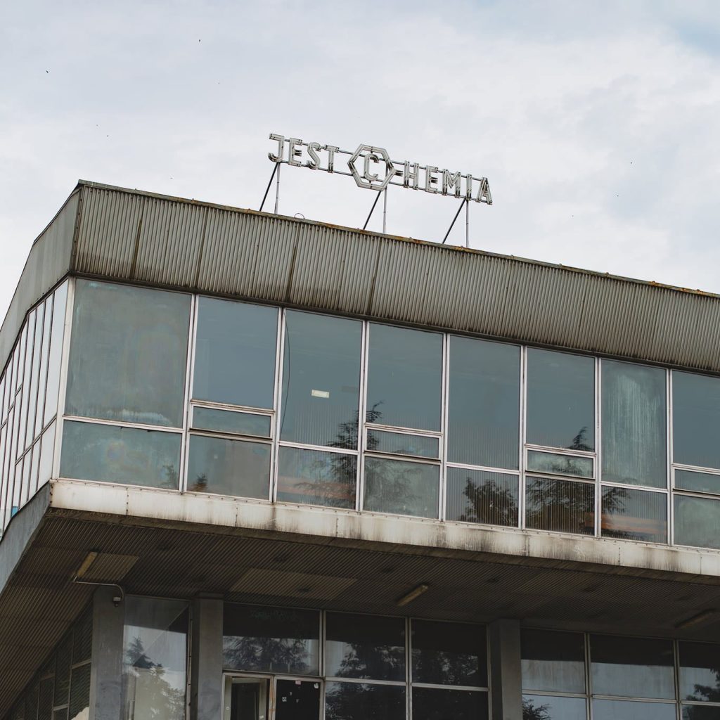 Kolorowa, kwadratowa fotografia przedstawiająca budynek Audytorium Chemii Uniwersytetu Wrocławskiego oraz neon na jego dachu.