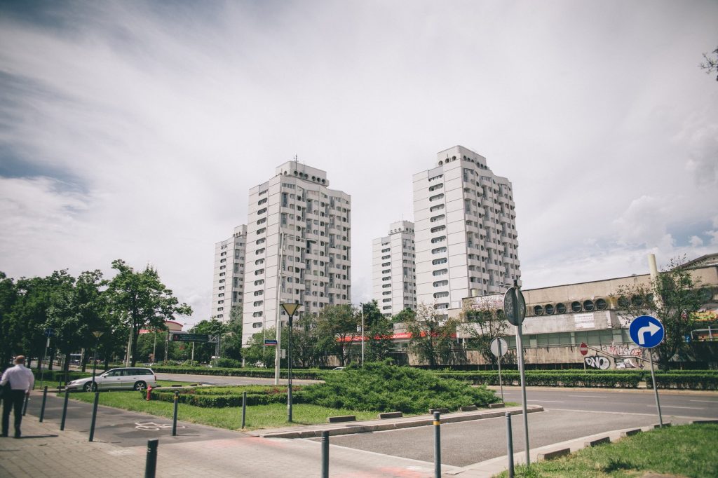 Widok na wrocławskie osiedle wieżowców - tzw. Manhattan. Nad zielonymi drzewami widoczne są szczyty białych budynków z charakterystycznymi zaokrąglonymi oknami.