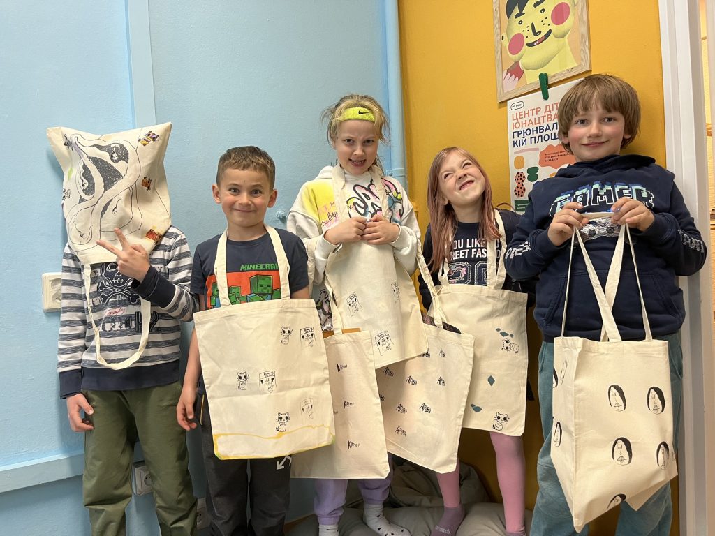 materiały organizatora Kolorowa, pozioma fotografia przedstawiająca pięcioro dzieci. Każde ma ze sobą własnoręcznie ozdobioną torbę. Dziecko z lewej strony założyło torbę na głowę. Reszta trzyma torby w rękach.