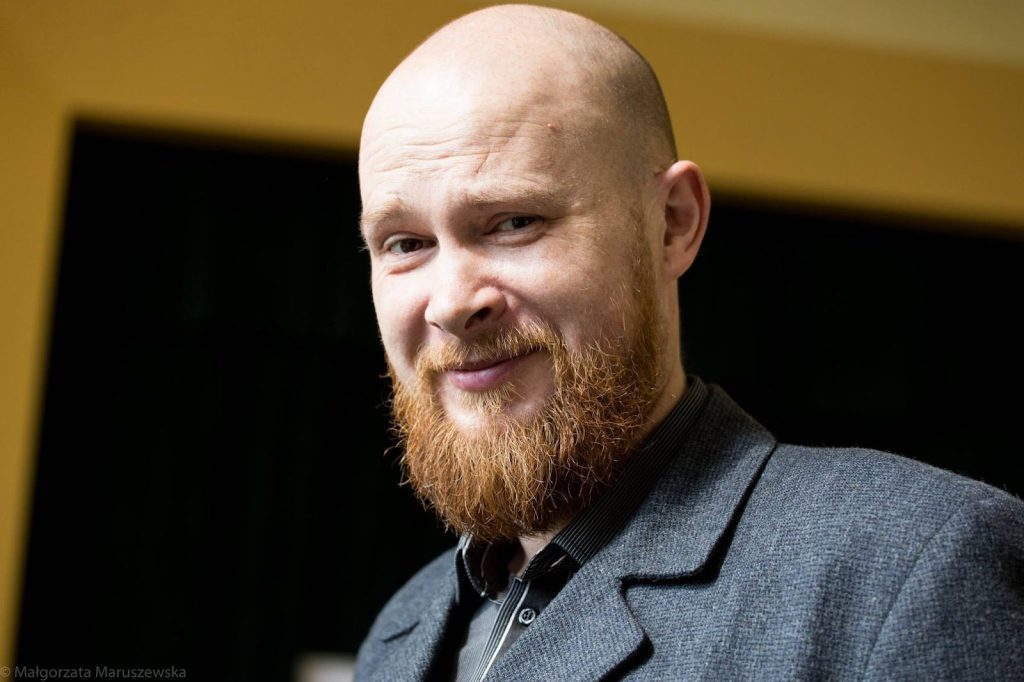 Kolorowa, pozioma fotografia przedstawia zbliżenie na twarz łysego mężczyzny z rudą brodą. To prowadzący spacery - Piotr Kmiecik.