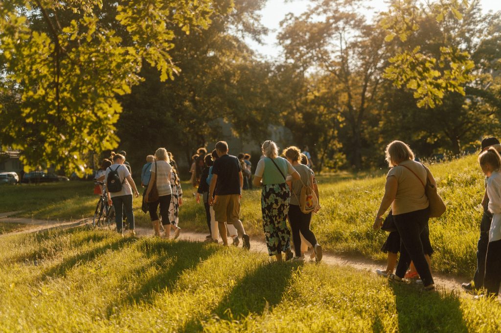 fot. Marcin Szczygieł Kolorowa, pozioma fotografia przedstawiająca grupę osób, spacerujących wąską ścieżką przez park.